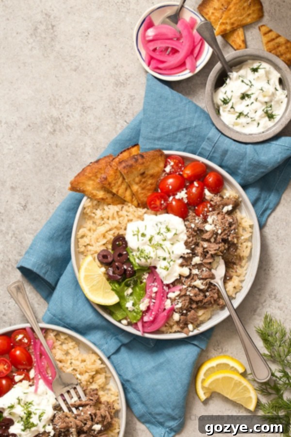 The finished Slow Cooker Gyro Rice Bowls, ready to be served, topped with fresh ingredients and tzatziki.