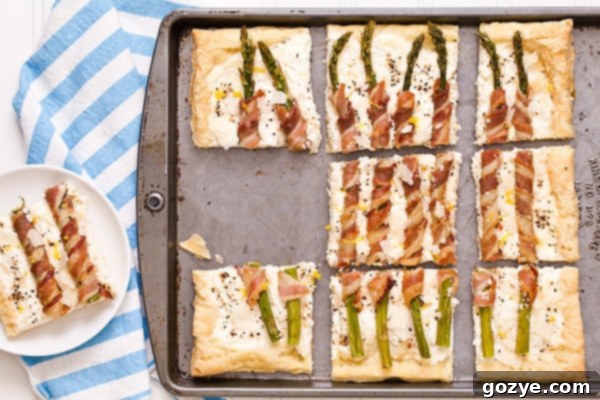 Flaky Asparagus and Bacon Puff Tart 4 Overhead view of the uncooked Bacon Wrapped Asparagus Puff Pastry Tart before baking, showing the ricotta filling and bacon-wrapped spears.