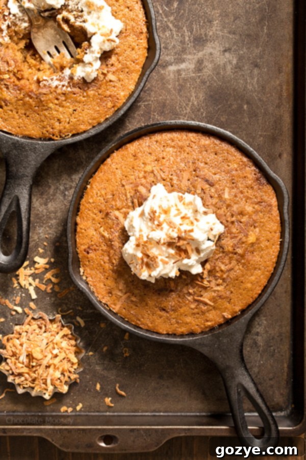 Two golden-brown Toasted Coconut Skillet Cakes, perfectly baked in cast iron skillets, ready to be served. The texture is invitingly moist and tender, hinting at the rich coconut flavor within.