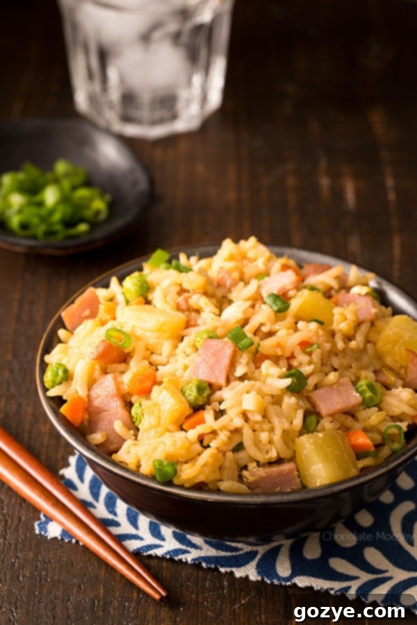 A vibrant bowl of Hawaiian Fried Rice, featuring savory ham, sweet pineapple tidbits, crisp peas, and carrots, garnished with fresh green onions. Perfect for using up leftover ham and a delicious alternative to Chinese takeout.