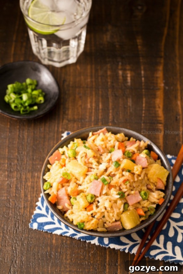 A cook's mise en place with all the ingredients for Hawaiian Fried Rice meticulously prepped and ready: diced ham, pineapple tidbits, chopped green onions, carrots, peas, ginger, and garlic, ensuring a smooth cooking process.