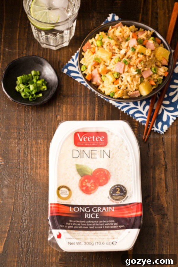 Close-up shot of Veetee Dine-In Long Grain White Rice being crumbled directly into a hot skillet, alongside sautéed vegetables, ready to be transformed into delicious Hawaiian Fried Rice, highlighting the convenience of quick-cook rice.