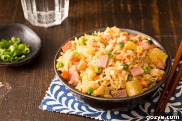 A generous serving of homemade Hawaiian Fried Rice with ham and pineapple in a white bowl, garnished with freshly chopped green onions, showcasing its vibrant colors and delicious texture. Ideal for a quick, satisfying meal.