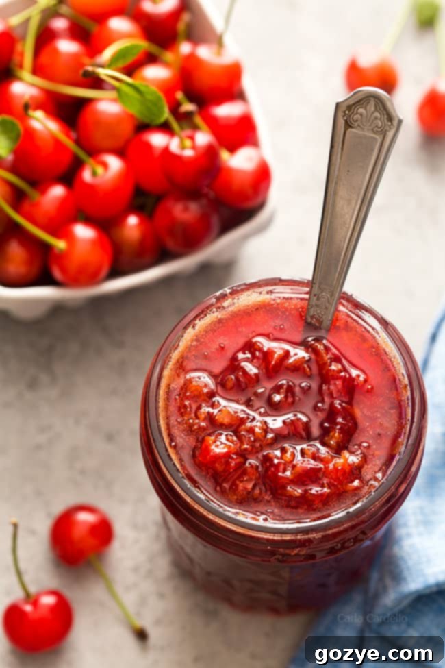 Pectin Free Small Batch Sour Cherry Jam 4 A small jar of homemade small batch sour cherry jam without pectin, with a spoon beside it, on a wooden board.