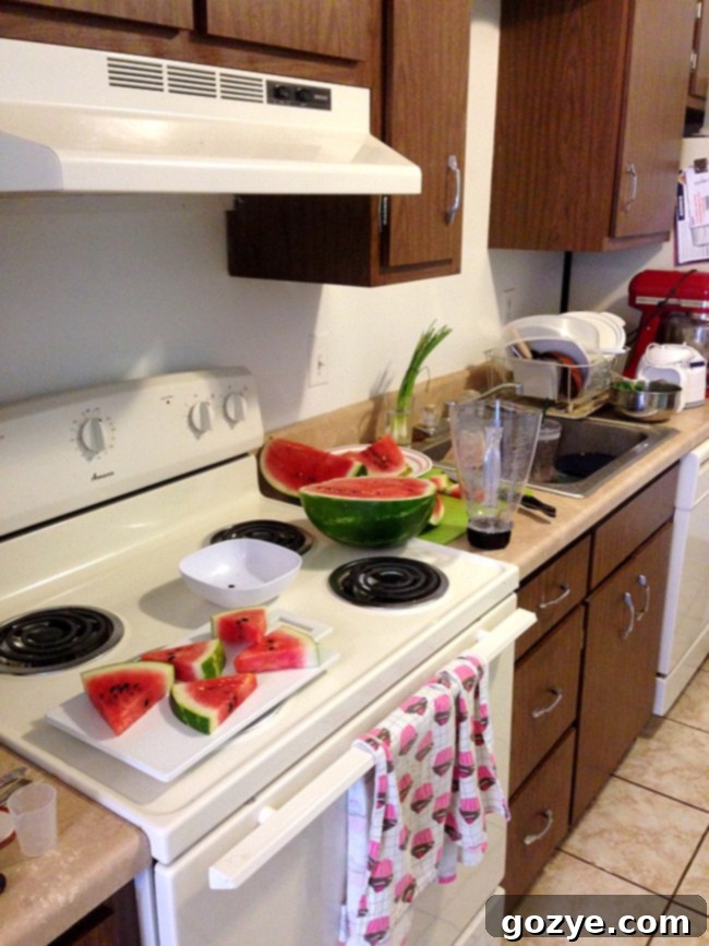 A person cutting a watermelon on a very small, crowded kitchen counter, illustrating the challenge of limited space in a tiny kitchen.