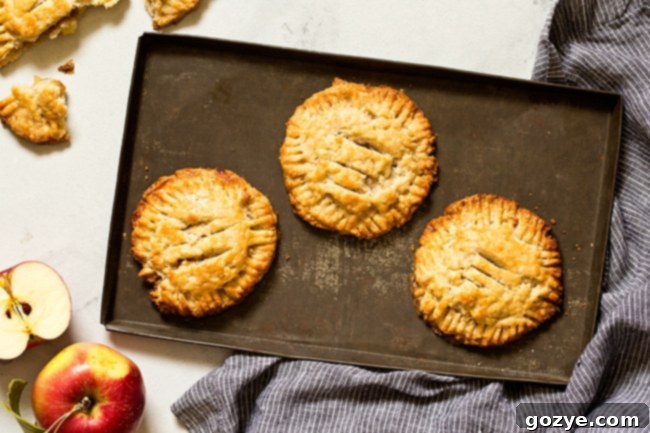 Overhead shot of two golden brown small batch apple hand pies, one sliced open to reveal the warm, spiced apple filling and flaky layers of crust.