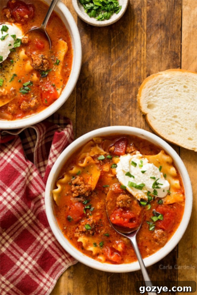 A close-up shot of a bowl of lasagna soup with a spoon, showing the melted cheese and noodles.