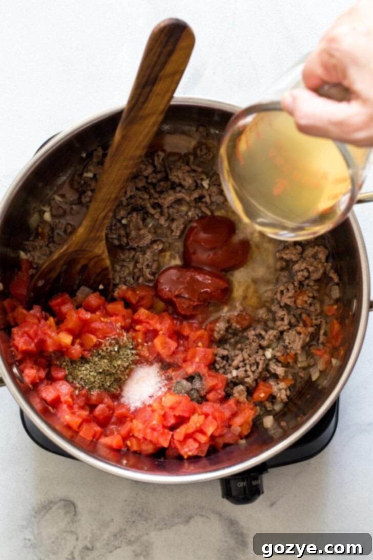 Adding broth and other ingredients to the browned ground beef and onions for lasagna soup.
