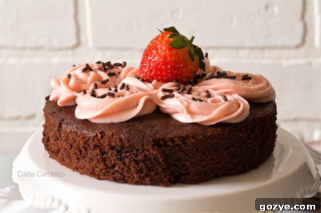 Close up of small chocolate cake with smooth pink frosting on a white cake stand