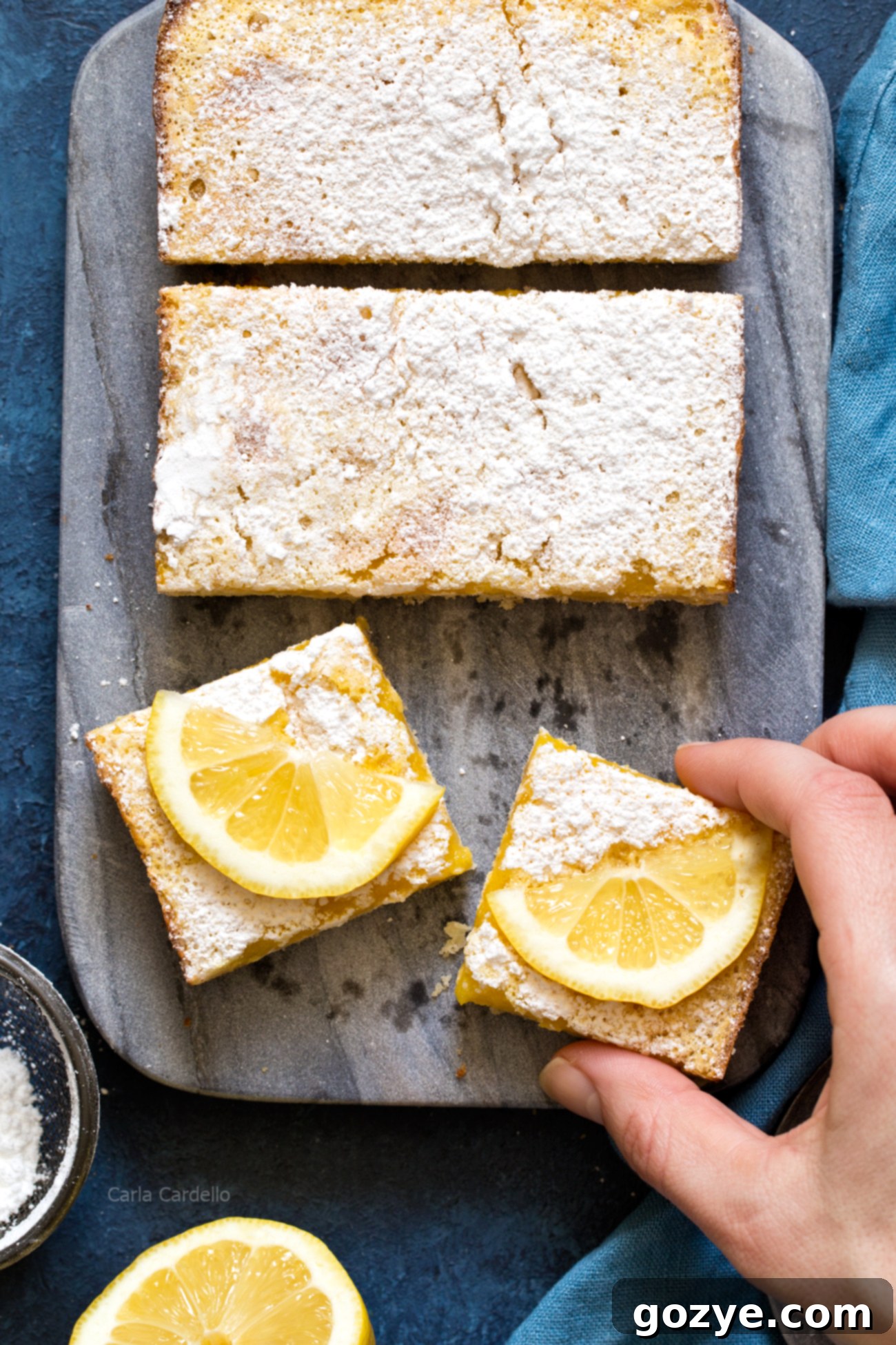 Zesty Small Batch Lemon Bars 3 A hand reaching for a freshly baked small batch lemon bar, still in the loaf pan, ready to be enjoyed