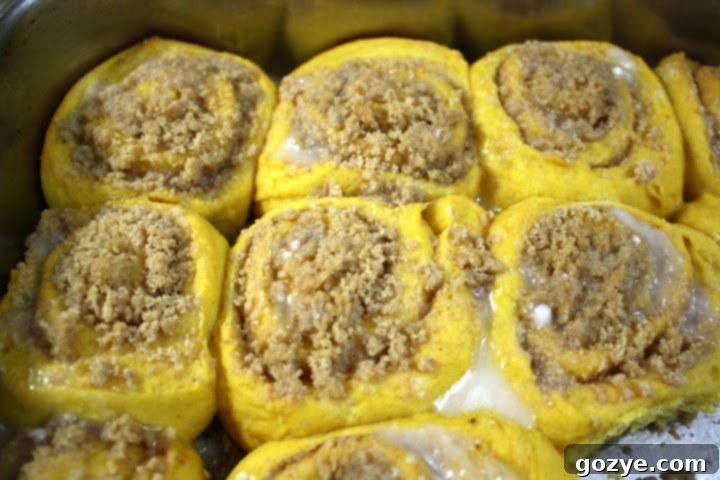 Close-up of golden brown Streusel Pumpkin Sweet Rolls with glaze in a baking dish