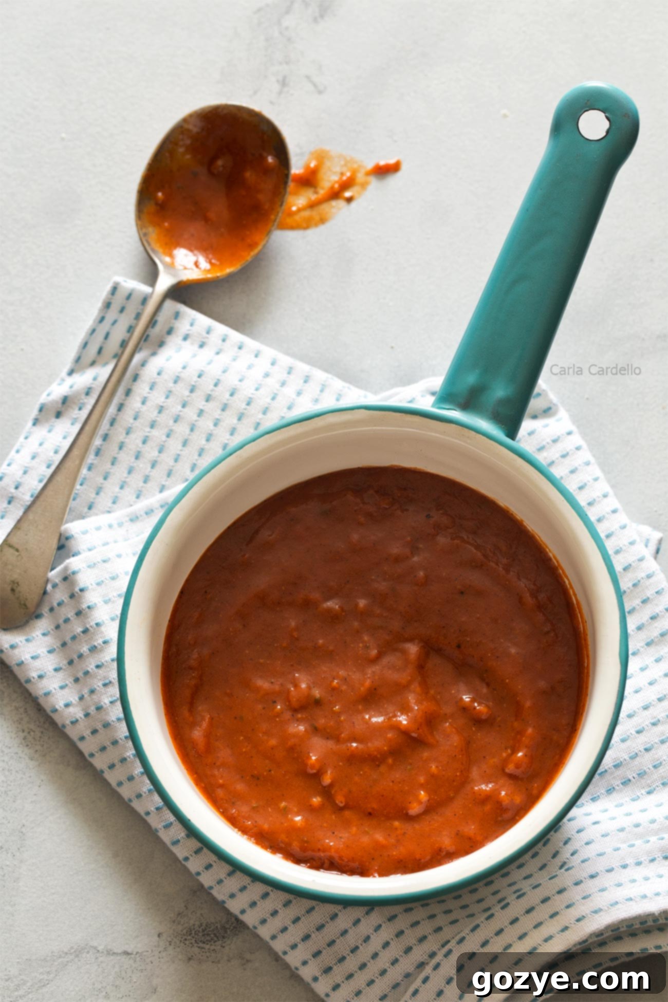 Homemade Red Enchilada Sauce simmering on the stove, covered to prevent splattering and thicken to the right consistency
