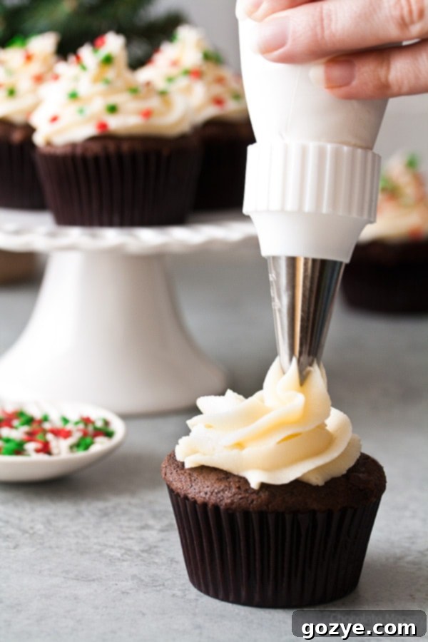 These small batch Chocolate Gingerbread Cupcakes with homemade cream cheese frosting makes a half dozen cupcakes. Ideal for when you want a small Christmas dessert without too many leftovers. Three cupcakes arranged on a rustic wooden board, showing the delightful sprinkles.