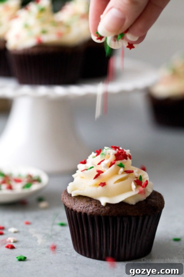 These small batch Chocolate Gingerbread Cupcakes with homemade cream cheese frosting makes a half dozen cupcakes. Ideal for when you want a small Christmas dessert without too many leftovers. A single cupcake held up, showing the fluffy frosting and colorful sprinkles.