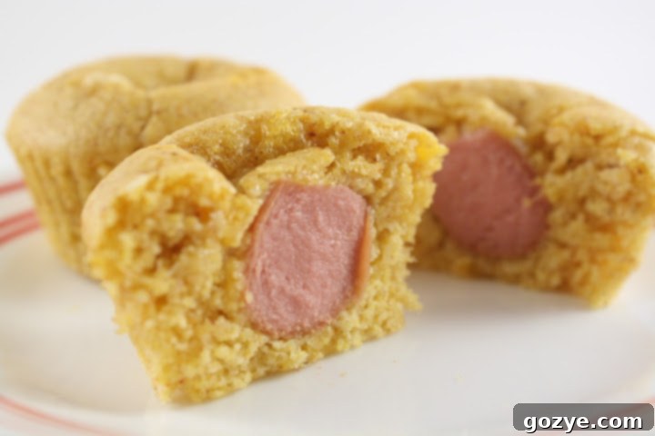 Freshly baked corn dog muffins arranged on a wire rack, showing golden-brown tops and a peek of the hot dog inside.