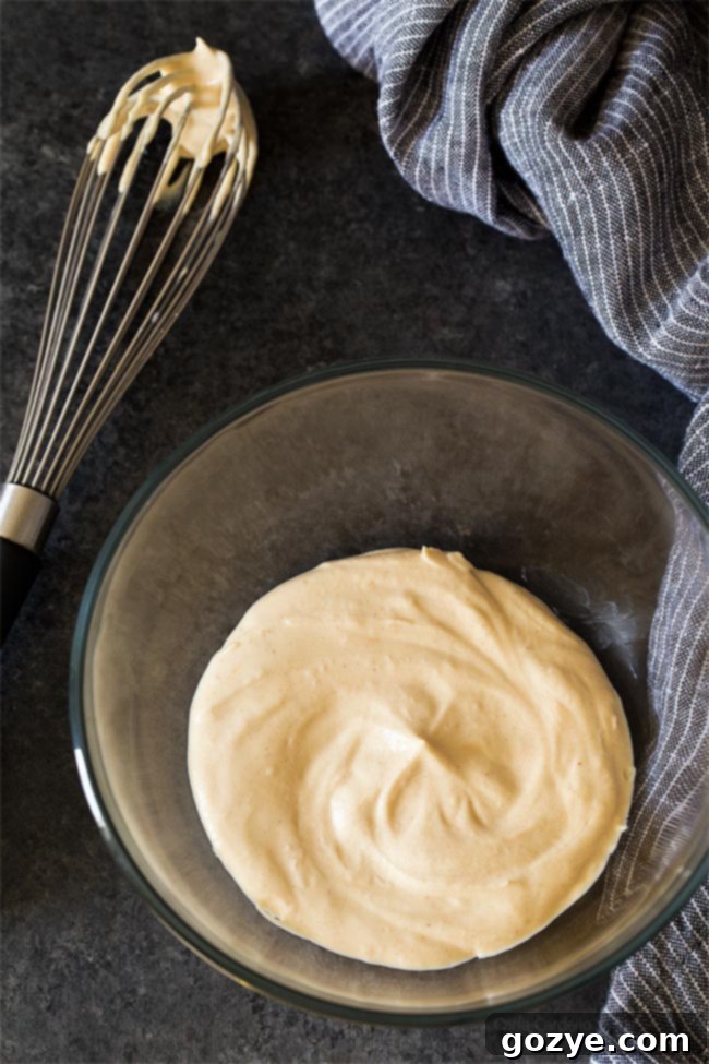 Peanut Butter Whipped Cream being whisked in a clear glass bowl, showcasing its creamy texture