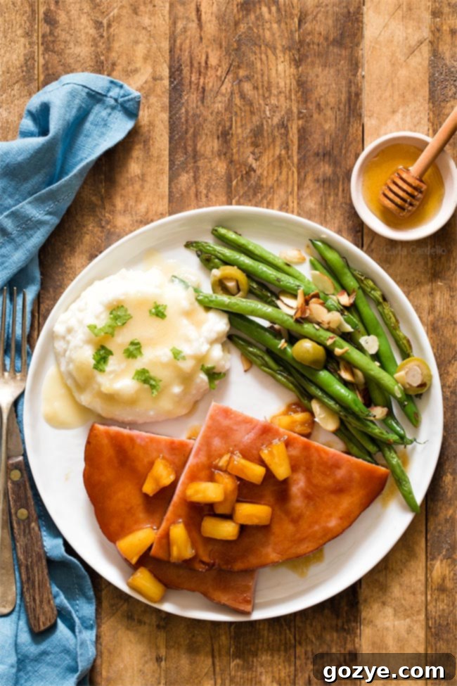 Easy Honey Glazed Ham Steak 3 Honey Glazed Ham Steak on a white plate with vibrant green beans and creamy mashed potatoes, ready to be served.