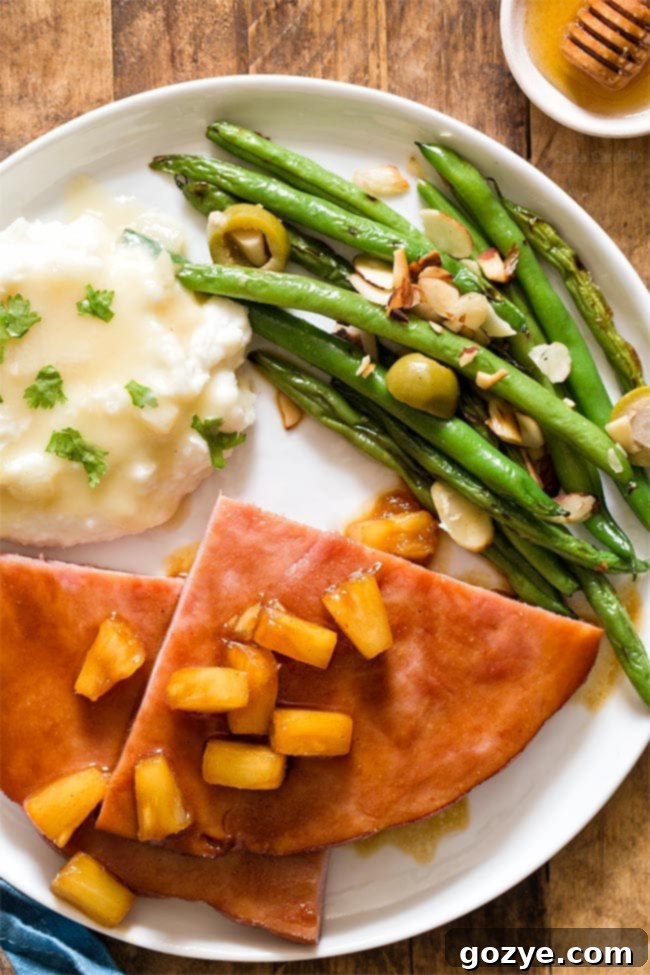Easy Honey Glazed Ham Steak 5 Honey Glazed Ham Steak with mashed potatoes and green beans on a white plate, showcasing the rich glaze.