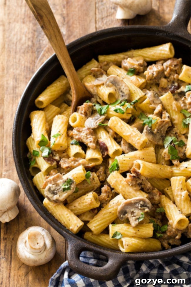 Pasta with sausage and Alfredo sauce with wooden spoon in cast iron pan