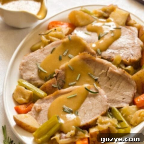 Sliced pork roast on white plate with vegetables and gravy