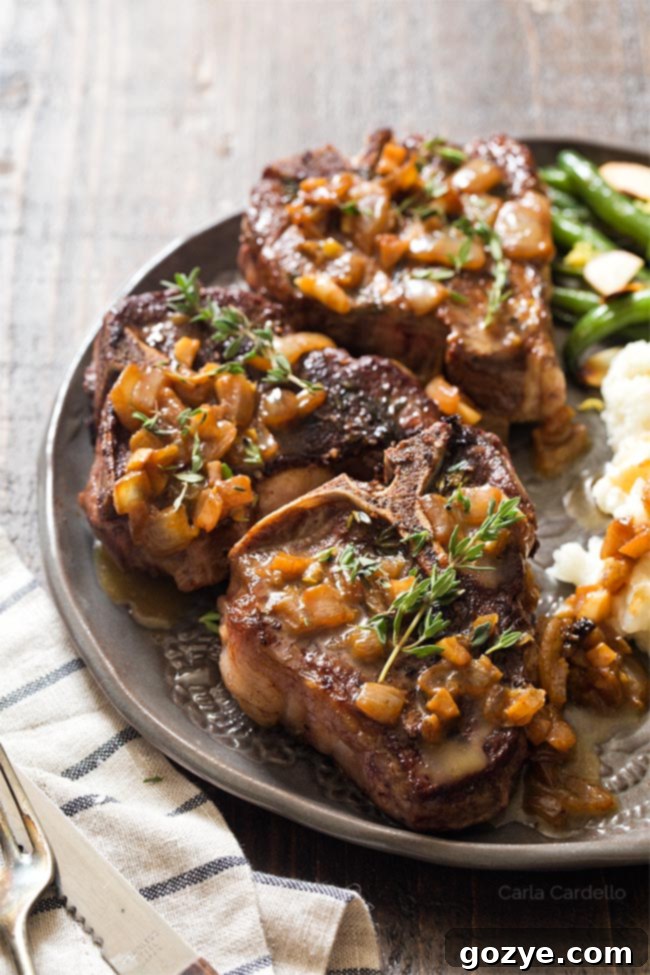 Lamb chops on plate with pan sauce, garnished with fresh herbs