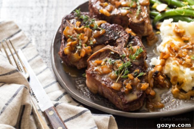 Perfectly fried lamb chops on a white plate, drizzled with pan sauce