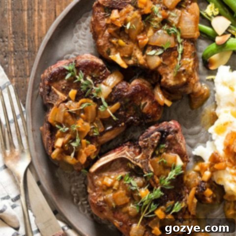 Pan fried lamb chops on gray plate with a side of sauce