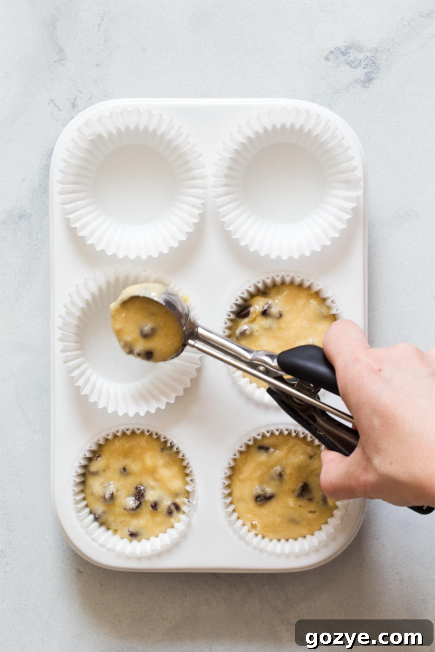 Scooping banana muffin batter into paper liners in a muffin pan