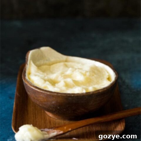 Homemade Coconut Buttercream Frosting in a brown coconut bowl, garnished with shredded coconut