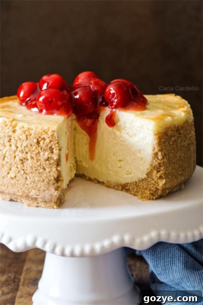 Close up of 6 Inch Cheesecake on white cake stand, garnished with cherry pie filling.