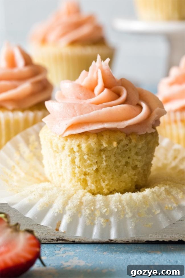 Beautifully frosted vanilla cupcake with its paper liner partially unwrapped, ready to be enjoyed.