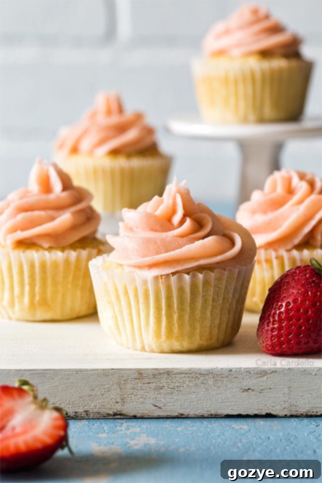 Three perfectly baked small batch vanilla cupcakes arranged on a white cutting board, showcasing their golden-brown tops.