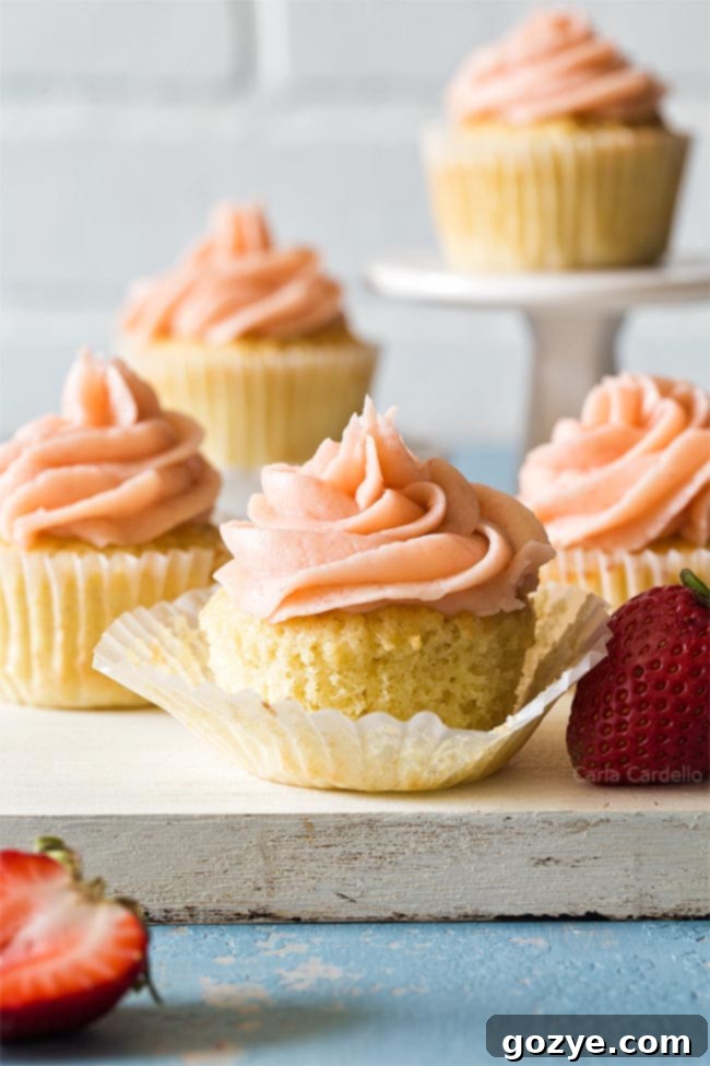 A trio of beautifully baked small batch vanilla cupcakes on a white cutting board, waiting to be frosted.