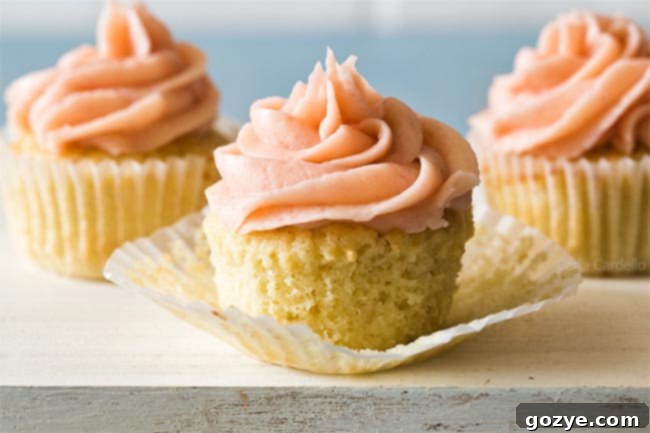 A single small batch vanilla cupcake, freshly baked and unfrosted, with its paper liner partially unwrapped.