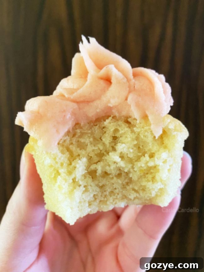A delicious small batch vanilla cupcake with a bite taken out, revealing its moist and fluffy interior.