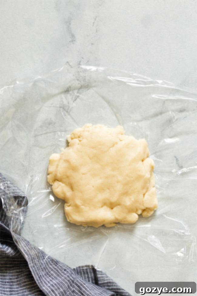 Pie dough wrapped in plastic wrap and shaped into a round disk