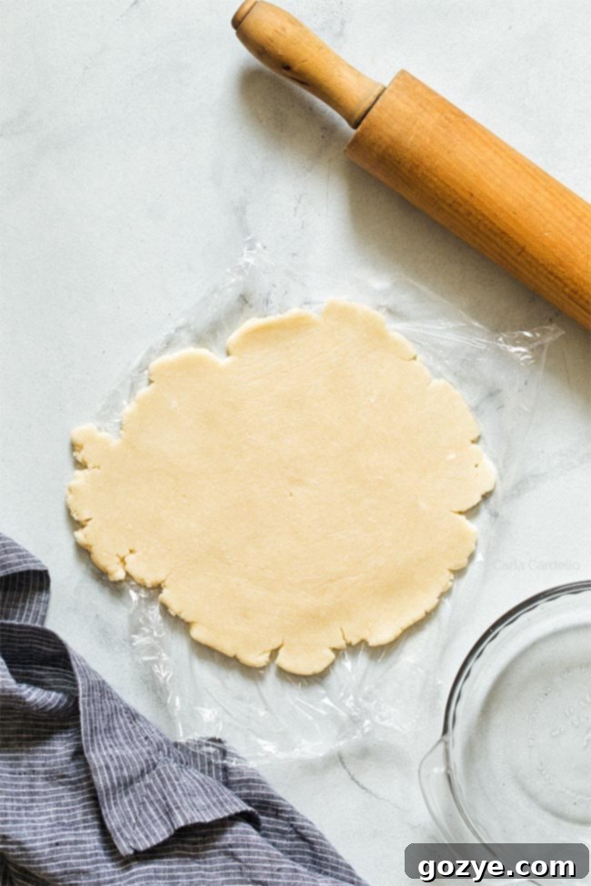 Rolling out pie dough between two sheets of plastic wrap with a rolling pin