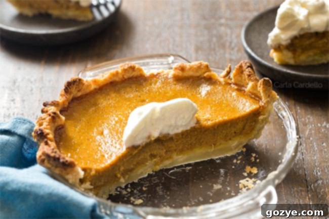 Half of pumpkin pie in glass pie pie with two slices on plates behind it