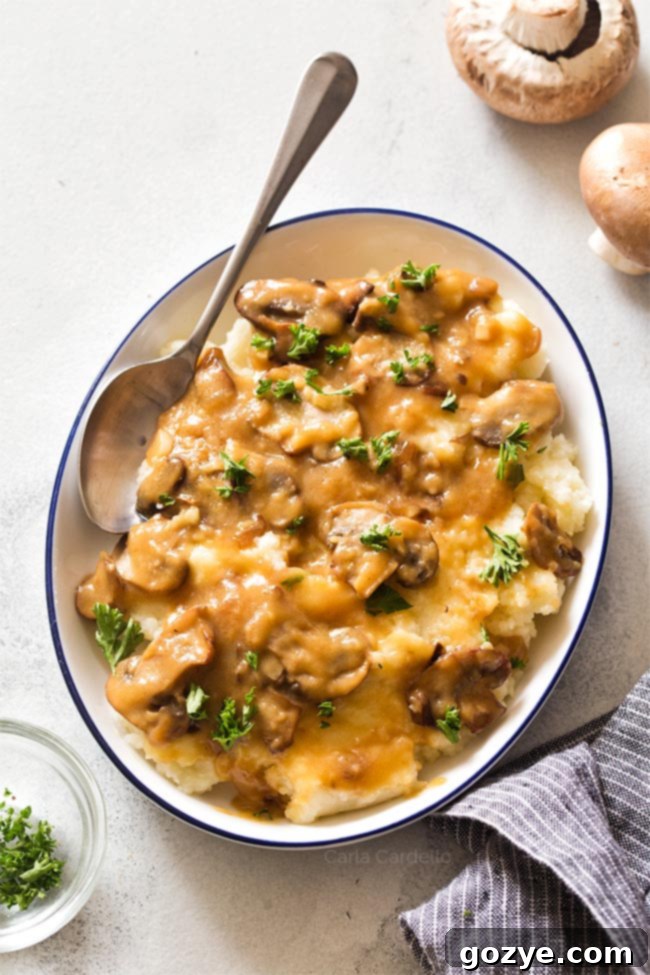 Brown mushroom gravy generously poured over creamy mashed potatoes on a white plate, ready to be enjoyed.
