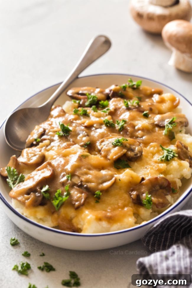 Rich brown mushroom gravy artfully poured over a bed of creamy mashed potatoes on a pristine white plate.
