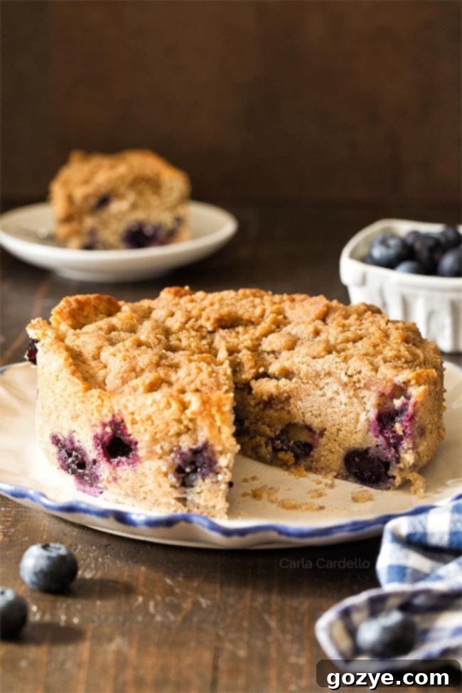 Small blueberry coffee cake on a white plate with a slice cut out, showcasing its fluffy texture and streusel topping