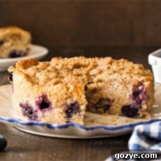 Small blueberry coffee cake on a white plate with a slice cut out, showing the crumb topping