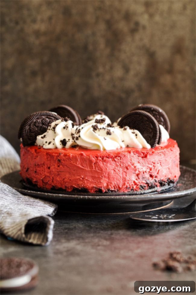 Luxurious Red Velvet Oreo Cheesecake adorned with fluffy whipped cream and scattered Oreo cookie pieces, resting on an elegant black plate, ready to be served
