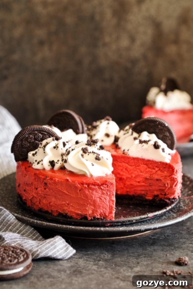 Close-up of a Red Velvet Oreo Cheesecake on a black plate, generously topped with swirling whipped cream and crunchy pieces of Oreo cookies, inviting a delicious bite