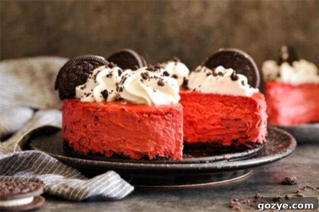 A second view of the Red Velvet Oreo Cheesecake with a missing slice on a black plate, highlighting the smooth texture of the cream cheese filling and the chunky Oreo crust