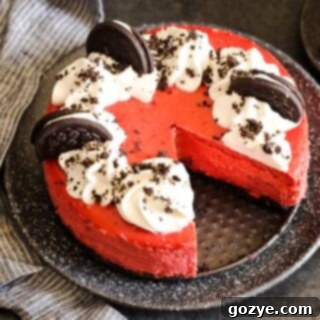 A slice of Red Velvet Oreo Cheesecake on a white plate, showcasing the rich red filling and dark Oreo crust, with an additional slice waiting to be eaten
