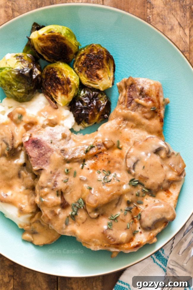 Close up of pork chop with gravy, mashed potatoes, and Brussels sprouts on a blue plate