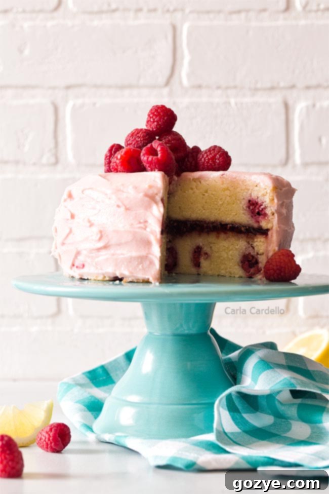 Bright lemon raspberry cake on a turquoise cake stand, garnished with fresh berries