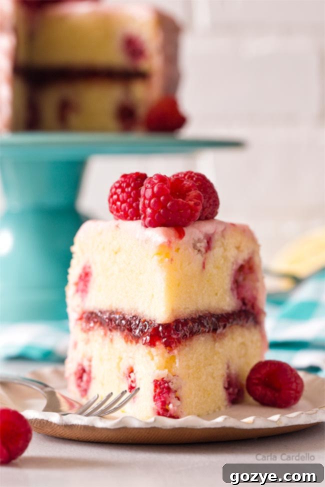 A slice of lemon raspberry cake on a white plate, showing the layers of cake, filling, and frosting
