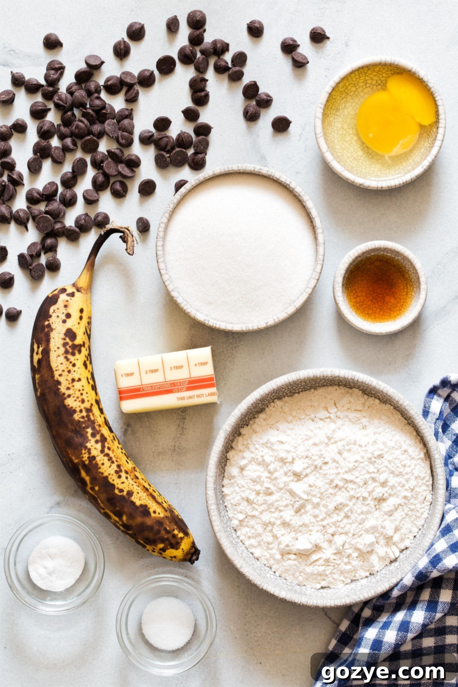 Petite Banana Bread Delights 5 A collection of ingredients laid out for making Mini Banana Bread: bananas, flour, sugar, butter, eggs, chocolate chips, vanilla, salt, baking soda